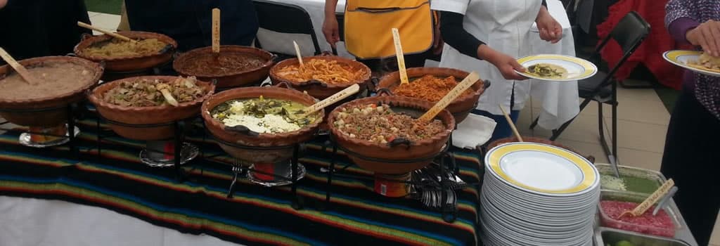 Panorámica de cazuelas de barro con guisados y tacos en una taquiza
